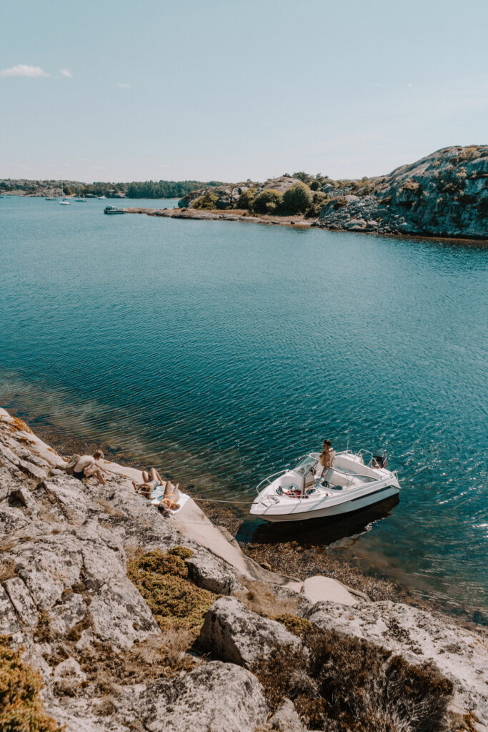 motor boat anchored by large rocks with people sunbathing on the rocks by the boat