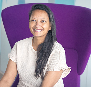 Christelle Paulley smiling, sat on a purple chair